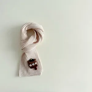 Detail of cream rib-knit kids scarf featuring a cute brown 3D bear patch decoration