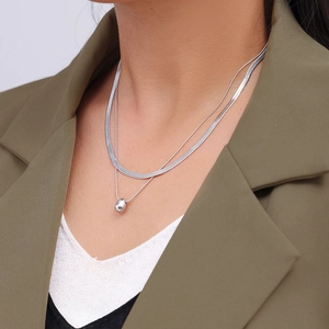 Silver layered necklace with snake chain and teardrop pendant on minimalist olive suit