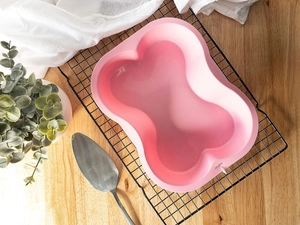 Pink silicone bone-shaped baking mold on a cooling rack over a rustic wooden table surface