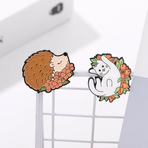 Detail of cartoon enamel pins featuring a brown hedgehog and white kitten on a grid stand