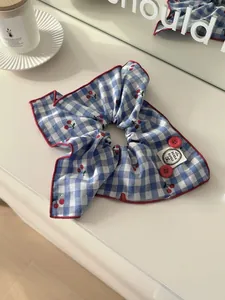Detail of blue and white checkered scrunchie with cherry print and handmade label