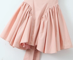 Detail showing the elegant pink pleated hem and premium satin fabric of the dress