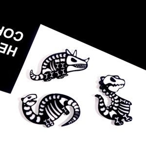 Détail de trois épingles à motif de squelette de dinosaure en émail noir et blanc