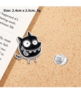 Detail shot of a black enamel monster pin on cork board with dimensions 2.4cm x 2.5cm