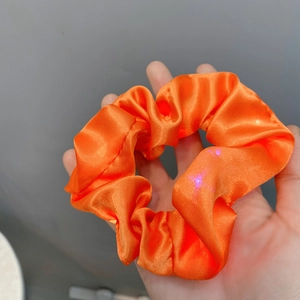 Macro detail of glowing orange satin LED scrunchie with purple lights on grey background