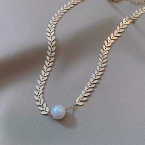 Close-up of gold wheat leaf chain necklace with a central white pearl detail