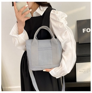 Detailed shot of a gray canvas tote bag featuring a front pocket and detachable strap