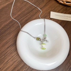 Détail du collier pendentif trognon de pomme avec perles vertes sur plateau céramique