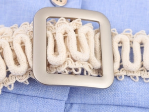 Detail van een beige gevlochten tailleriem met een matte metalen gesp op een blauwe jurk