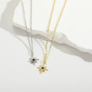 Minimalist gold and silver starfish pendant necklace with black gemstone on white stone background