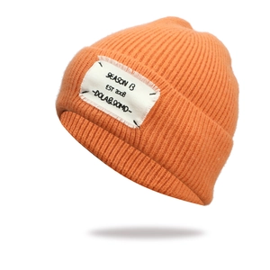 Detail of orange knit beanie with white SEASON B patch and textured knit fabric style