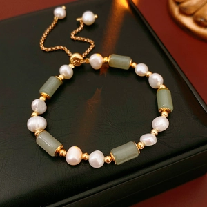 Detail of pearl and green jade bamboo bead bracelet with gold accents on black leather