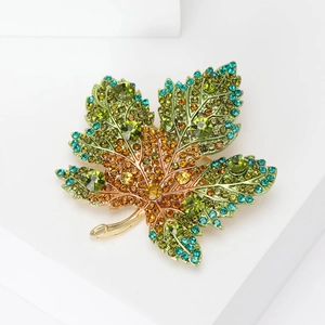 Close-up of maple leaf brooch with green and yellow gradient rhinestones on white stand