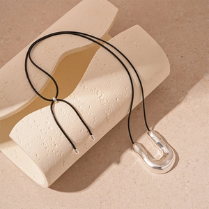 Macro view of a silver liquid-textured U-shape metal pendant on a black cord necklace