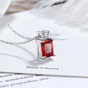 Macro detail of rectangle red zircon pendant with silver cross chain on white card