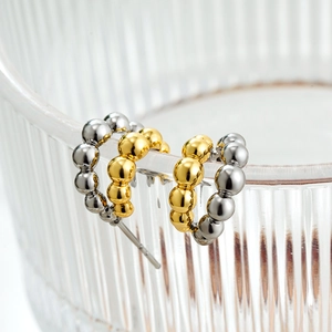 Macro shot of gold and silver beaded C-shaped hoop earrings on glass rim