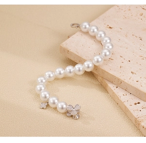 Detail of silver clover pendants and pearls on a textured beige stone surface