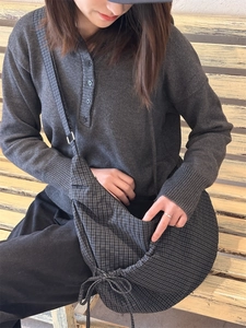 Detailed view of grey plaid crossbody bag with side drawstring worn in a casual setting