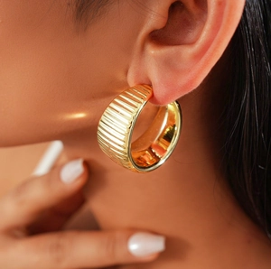 Close-up of golden chunky C-shaped hoop earrings with ribbed texture on a female model