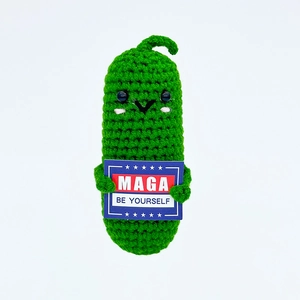 Macro shot of handmade crochet green pickle doll holding a blue motivational MAGA card