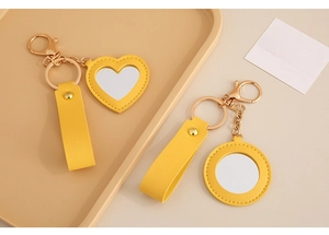 Close-up of yellow PU leather heart and round mirror keychains with fine stitching details