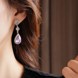 Close-up of vintage teardrop purple gemstone earrings with silver floral diamond settings