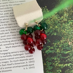 Close-up of resin berry drop earrings in red and green on vintage paper background