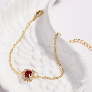 Détail macro du bracelet doré orné de zircon rouge posé sur une assiette en céramique