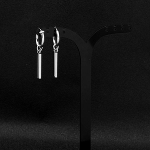 Macro shot of silver stainless steel hoop earrings with long bar charms on black stand