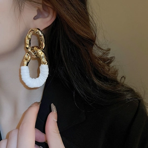 Détail d'une boucle d'oreille ovale en métal doré avec une texture en cuir blanc enroulé