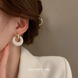 Close-up of elegant gold buckle white circle earrings worn by a female model