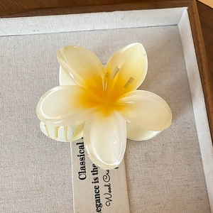 Close-up of yellow and white gradient lily flower hair claw clip on a linen tray