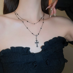 Dettaglio di collana gotica con croce d'argento e perline nere su doppia catena