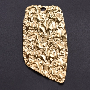 Macro shot of irregular heart pendant with hammered gold texture on grey background