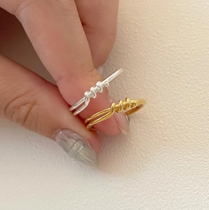 Detail view of gold and silver minimalist knotted twist rings held on neutral background