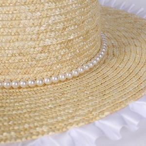 Close-up of woven straw hat featuring white lace trim and delicate pearl beads