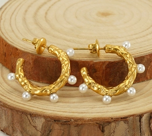 Gros plan sur des boucles d'oreilles dorées en C avec texture martelée et perles blanches