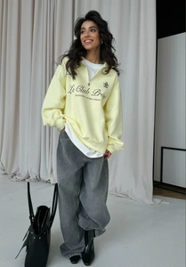 Detail of light yellow half-zip sweatshirt with letter print and grey wide-leg jeans