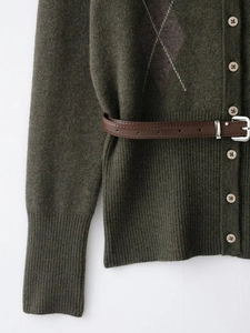 Détail du cardigan en maille vert foncé avec motif losanges violets et ceinture en cuir