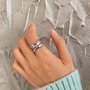 Close-up of wavy multi-layer silver 925 ring on hand against a grey textured background