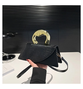 Detail of glossy black crocodile pattern bag with a gold sculptural handle and strap