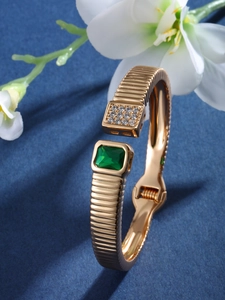 Close-up of golden spring cuff with green gemstone and diamond accents on blue background