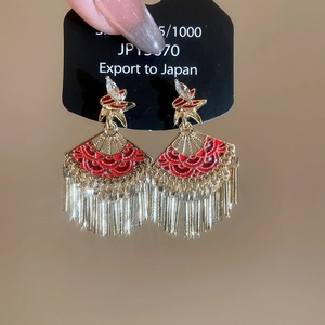 Detailed macro shot of red enamel fan earrings with golden tassels and sparkling rhinestones