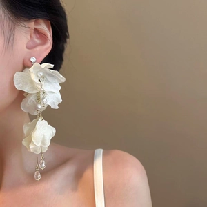 Close-up of elegant white fabric flower earrings with long shimmering silver tassels