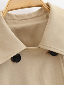 Close-up of khaki trench coat collar and black buttons showing twill fabric texture