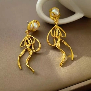 Macro detail of golden metal bow drop earrings featuring elegant white pearls on top