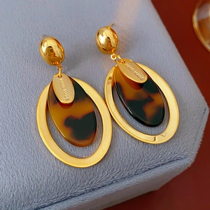 Detail of gold-plated resin oval earrings with handmade tag on velvet box