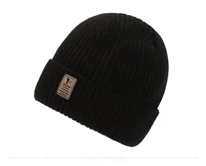 Close-up of black ribbed knit beanie with brown leather patch on white background