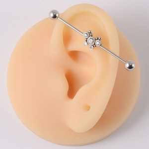 Close-up of silver steel industrial barbell with crystal flower design on a silicone ear model