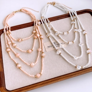 Detail of multi-layer pearl necklace with flower accents on a wooden tray with soft lighting